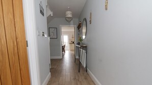 A hallway with wooden flooring, a wooden door, and a table with a mirror and vase. - The Hideaway Beach House (New Romney)