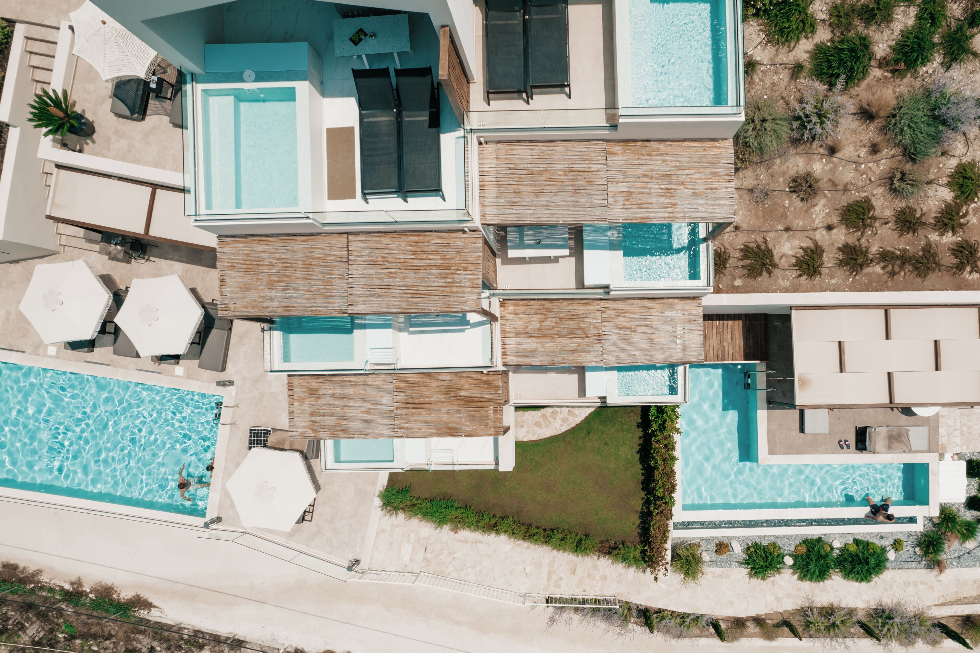 A modern multi-level residential building with a large swimming pool, outdoor seating, and a landscaped garden.