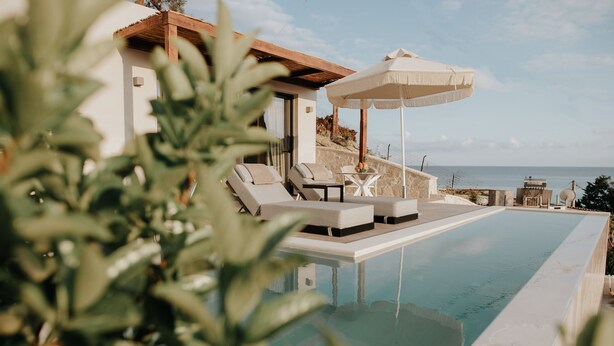 Zona junto a la piscina con sillones de descanso y una mesa, con vista al mar.