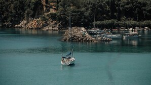 Un lago tranquilo con un velero en primer plano y varios barcos amarrados en la orilla.