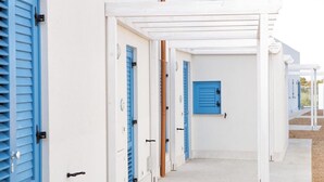 A corridor with white walls and blue doors, leading to a covered area with a white pergola. - Holiday Home in Favignana near Beach (Favignana)