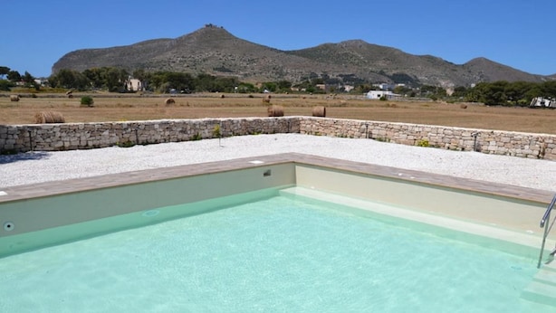 A swimming pool with a stone wall and a mountain in the background. - Holiday Home in Favignana near Beach (Favignana)