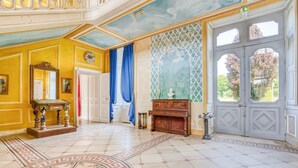 Una sala imponente con un espejo grande y ornamentado, una chimenea y un ventanal con vistas a árboles.