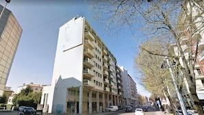 Ein mehrstöckiges Gebäude mit Balkonen, eine Straße davor und geparkte Autos.