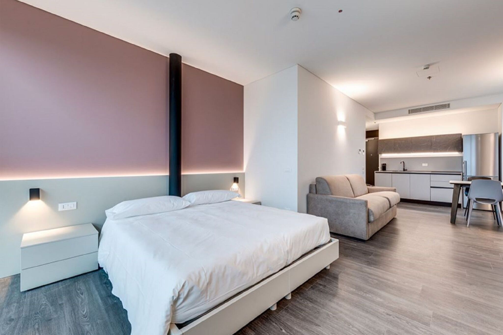 Una habitación de hotel moderna con una cama grande, un sofá, un escritorio y una kitchenette.