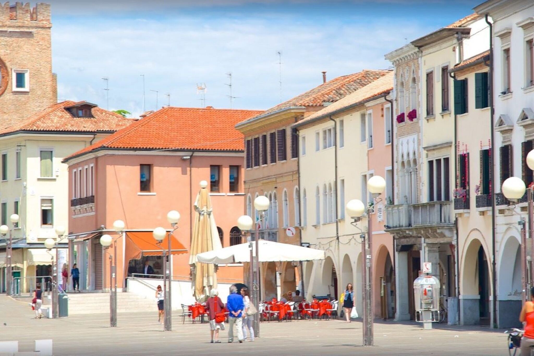 Une place agrémentée de terrasses, bordée de bâtiments historiques et surmontée d’une tour.