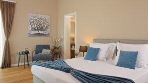 Una habitación de hotel con una cama, una silla, una mesita, un cuadro y una puerta que da al baño.