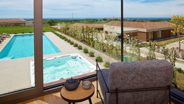 Balcón con vista a una piscina y un jacuzzi, una silla y una mesita con tetera y taza.