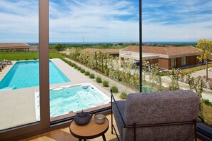 Balcón con vista a una piscina y un jacuzzi, una silla y una mesita con tetera y taza.