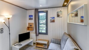 A modern living room with a flat-screen TV, a grey sofa, and a small wooden shelf. - Serene Chalet in Hourtin near Lake (Hourtin)