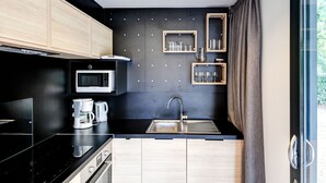A modern kitchen with a black countertop, stainless steel appliances, wooden cabinets, and a window with curtains. - Serene Chalet in Hourtin near Lake (Hourtin)