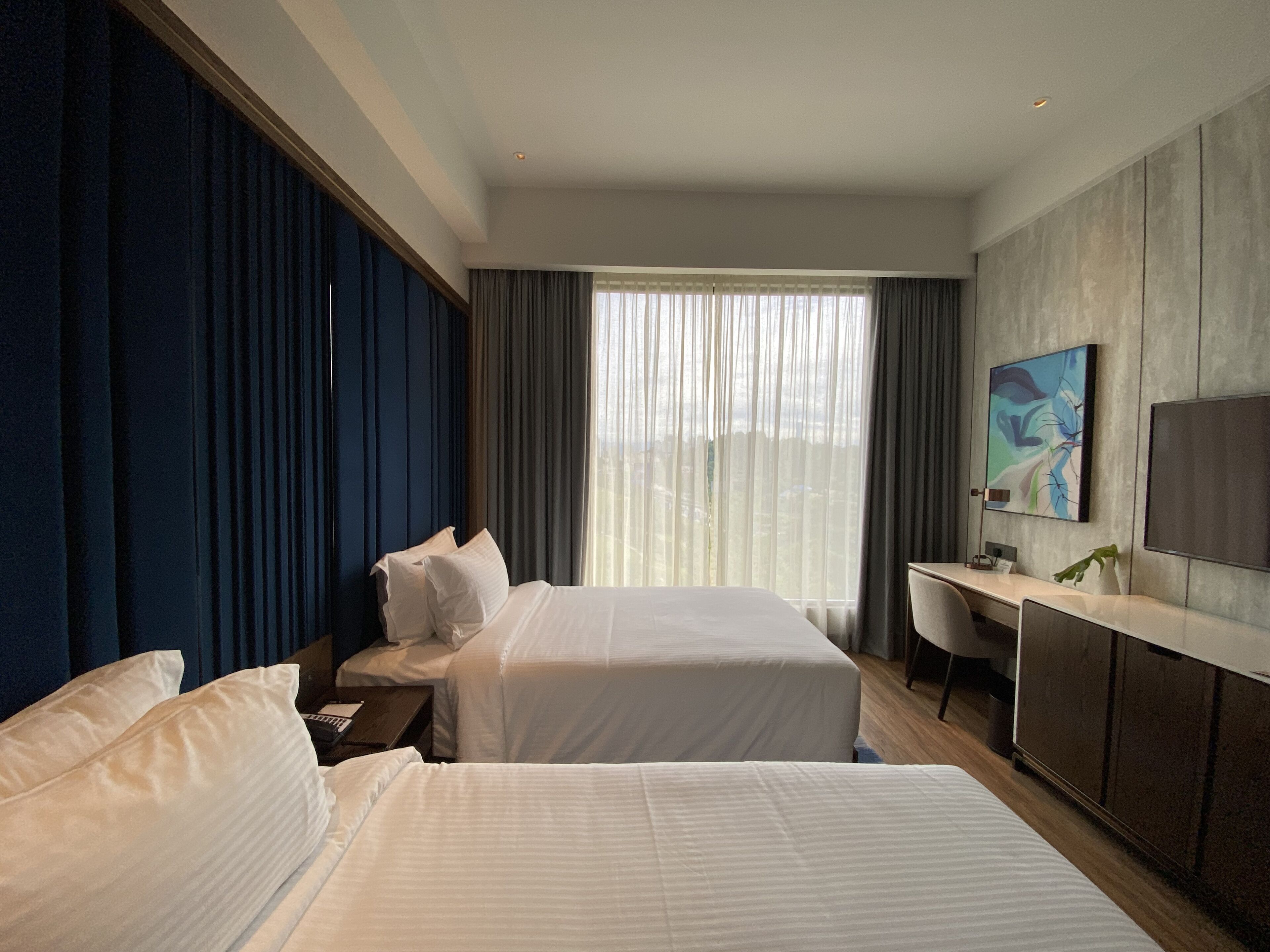 A hotel room with two beds, a desk, a chair, and a TV.