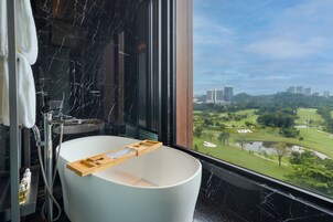 A modern bathroom with a bathtub, a shower, and a large window offering a view of a golf course and cityscape.
