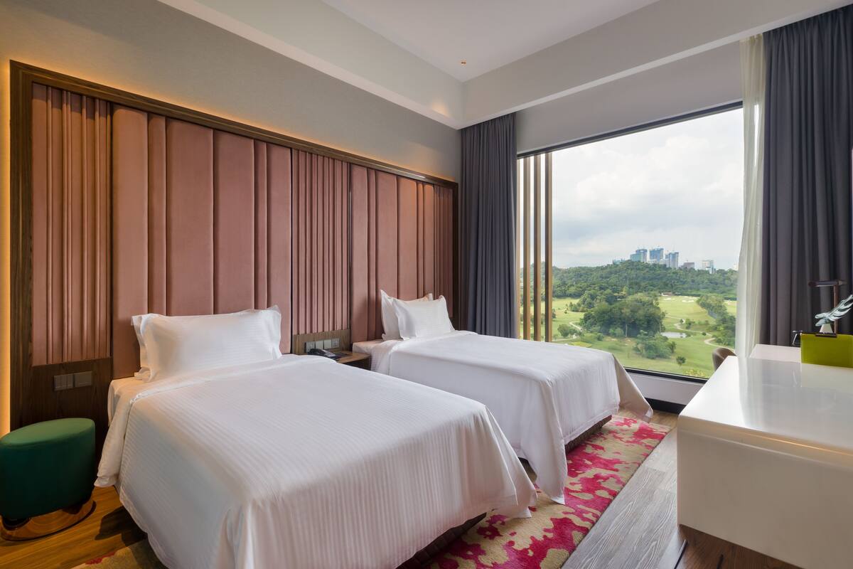 A hotel room with two beds, a desk, and a view of a cityscape.