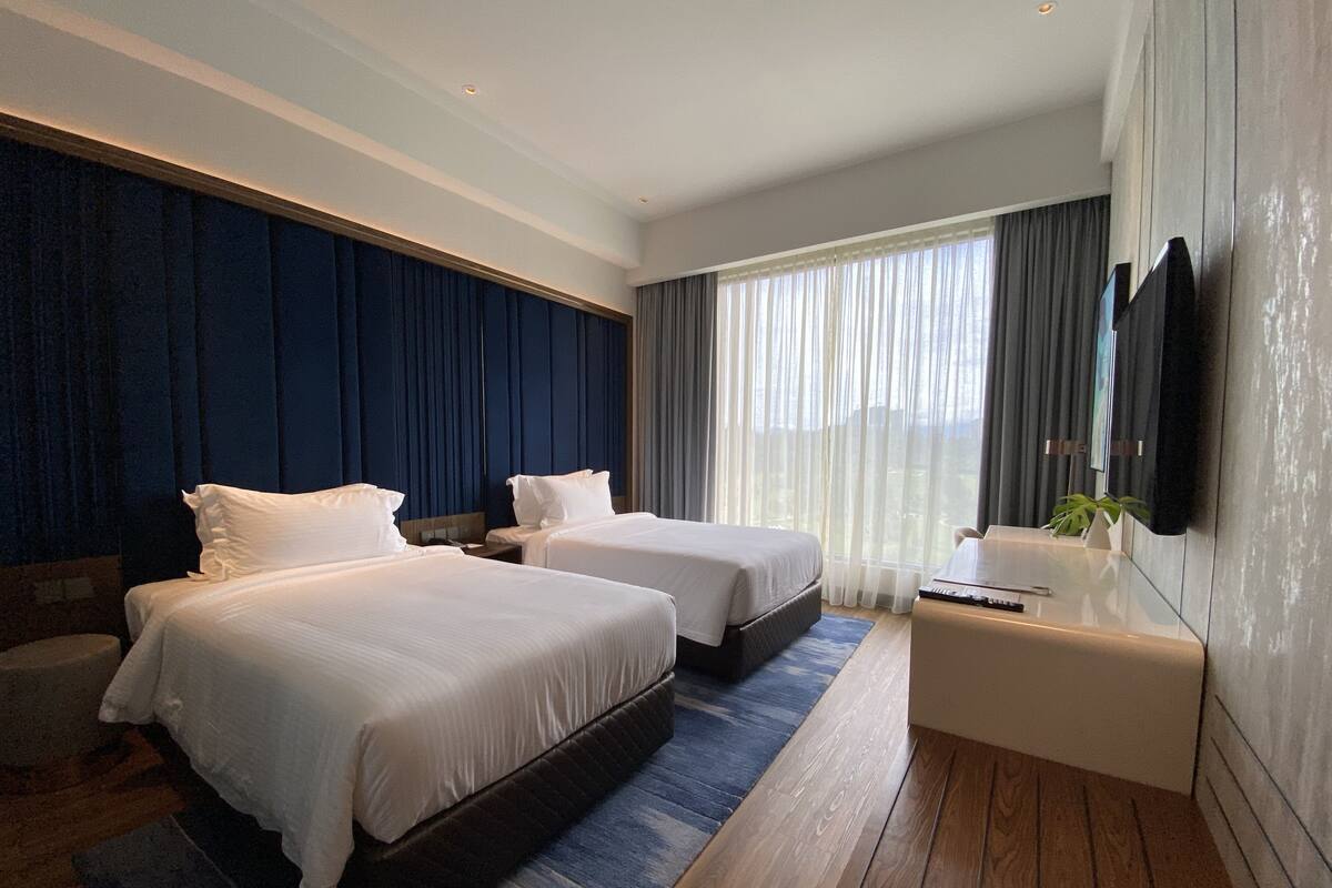 A modern hotel room with two beds, a desk, and a large window with curtains.
