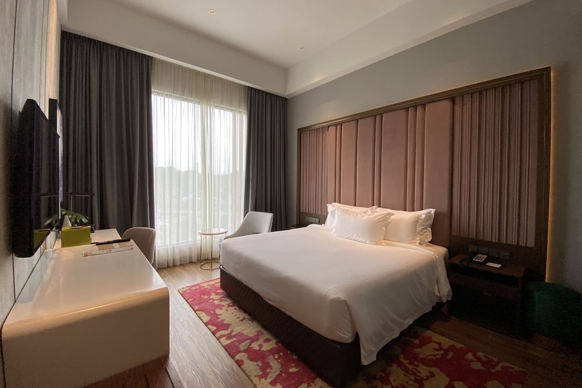 A hotel room with a large bed, a desk, a chair, a small table, and a TV.