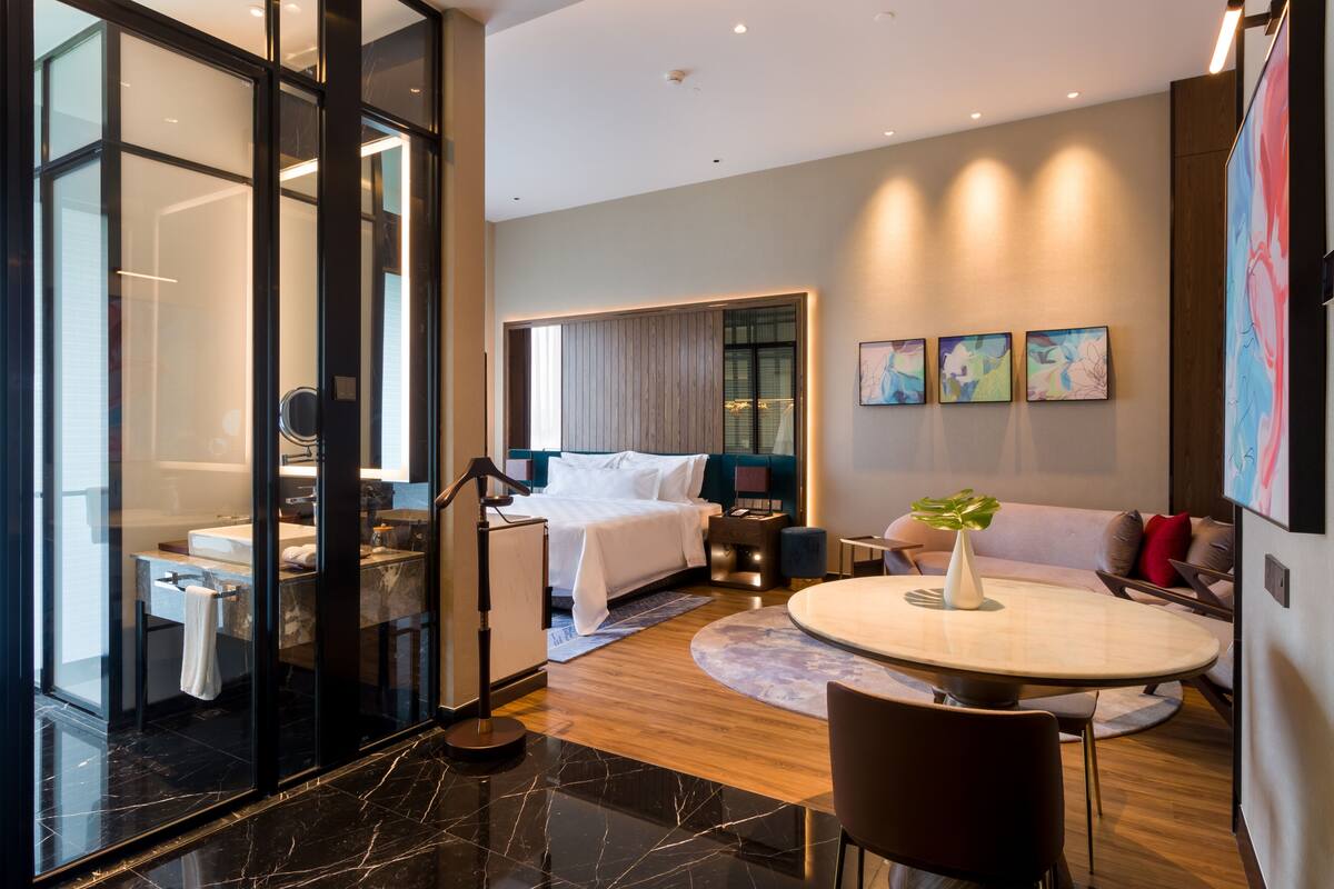A modern hotel room with a bed, a desk, a round table, and a sofa.