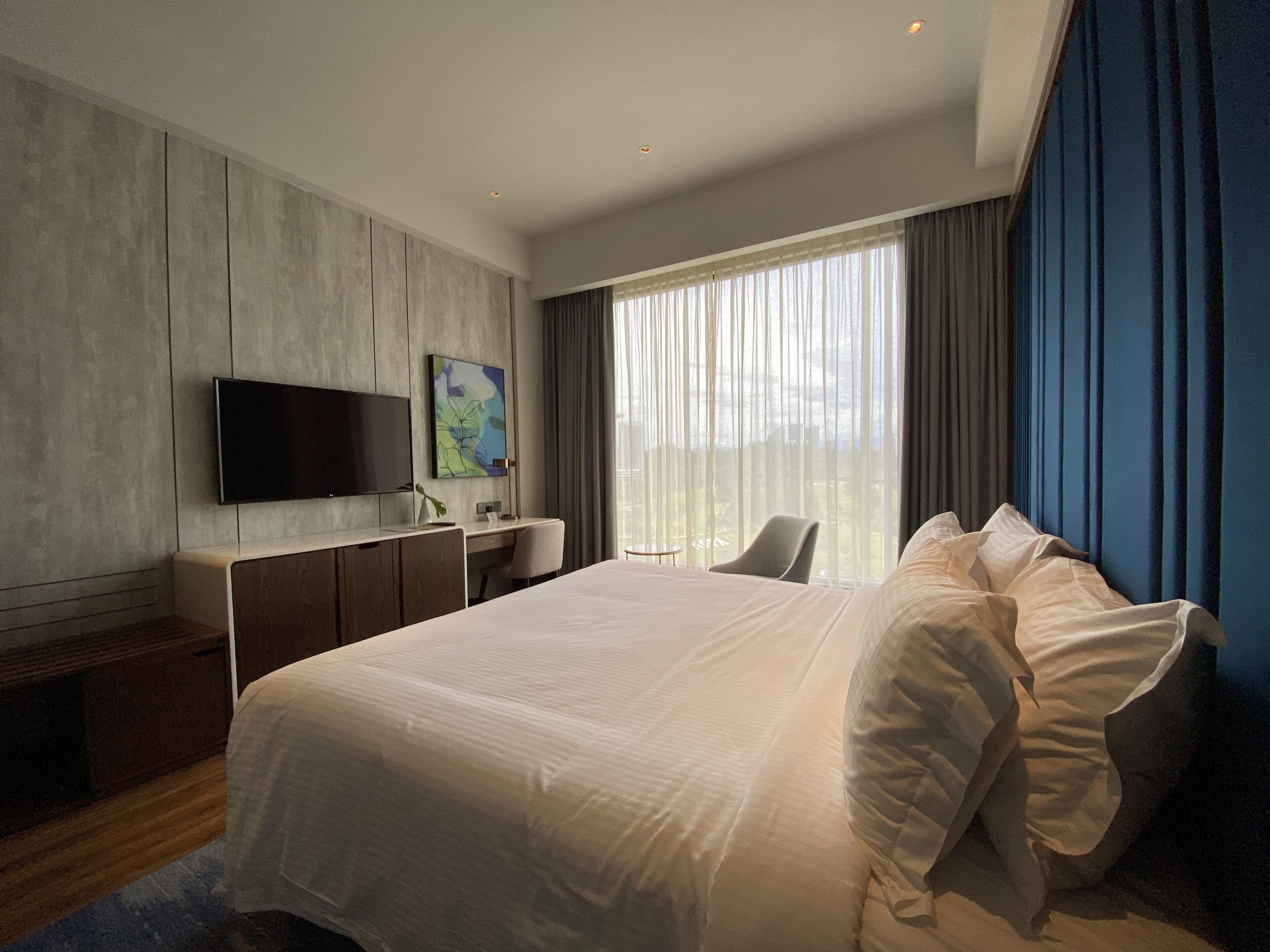 Camera d'albergo moderna con un letto grande, una scrivania, una sedia, una TV a schermo piatto e una finestra con tende.