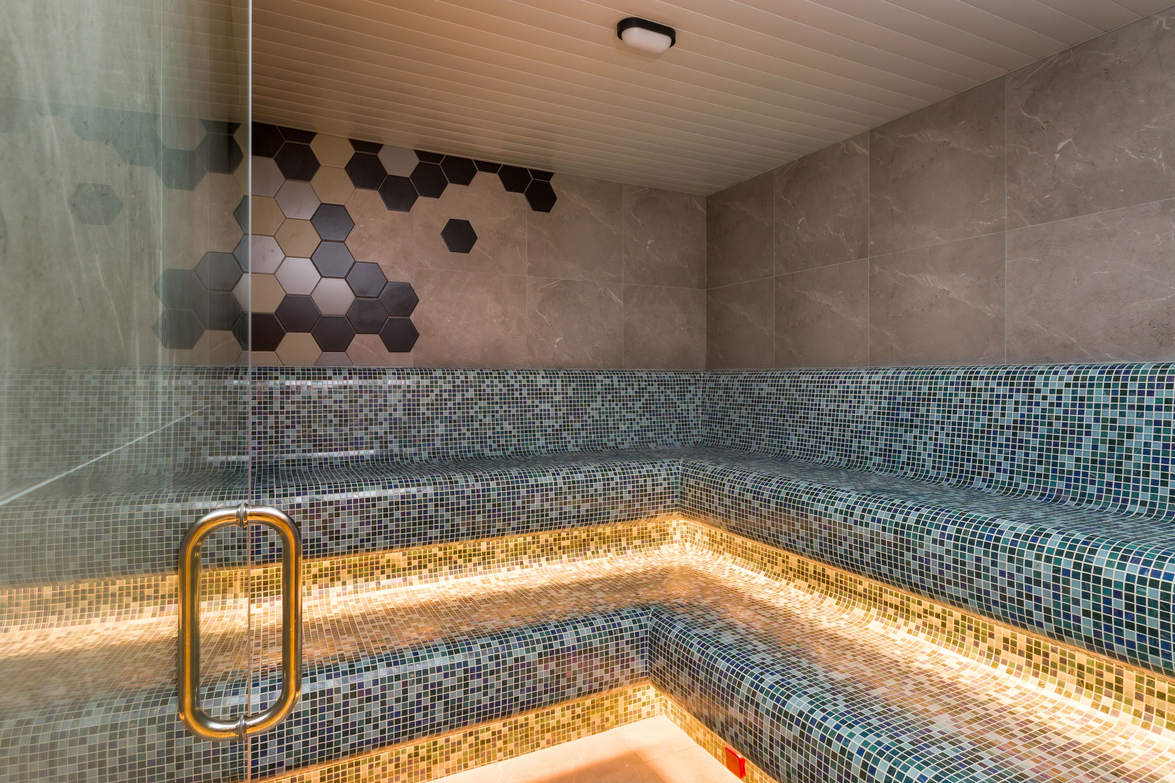 A modern bathroom with a glass partition, a mosaic-tiled bench, and a wooden ceiling.