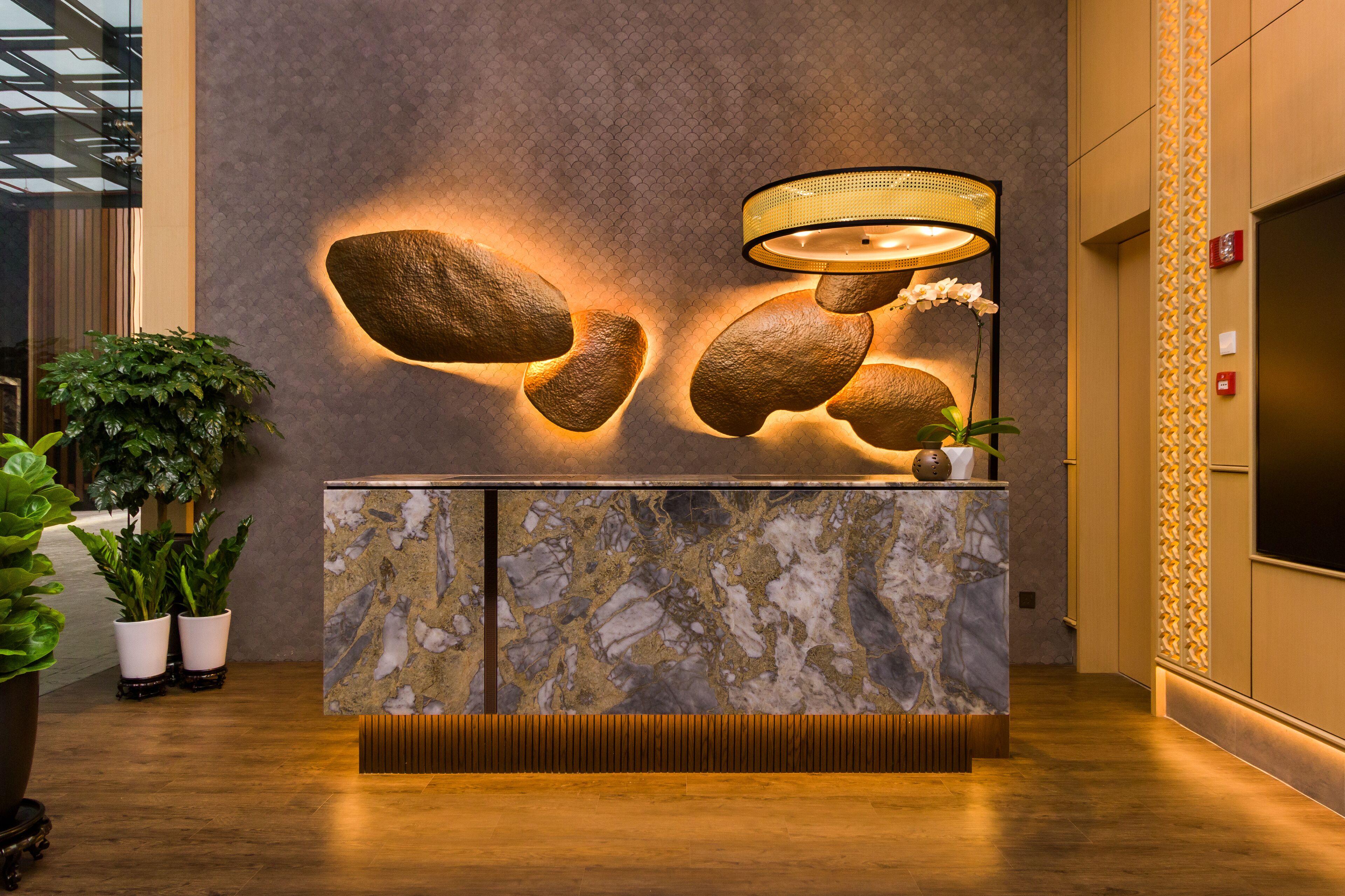 A reception desk with a marble top, a wall-mounted lamp, and potted plants.