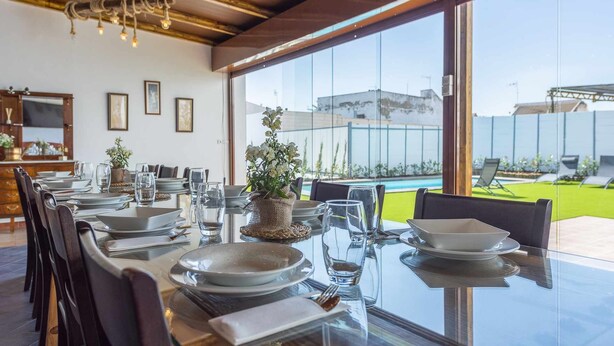 A dining area with a glass table, chairs, and a view of a swimming pool and greenery. - Rural House Maimones. (Los Pérez)