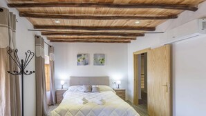 A bedroom with a wooden ceiling, a bed with a white quilt, two bedside tables with lamps, and a wooden wardrobe. - Rural House Maimones. (Los Pérez)