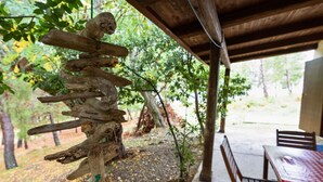 A rustic outdoor seating area with a wooden table and chairs, surrounded by trees and a covered structure.