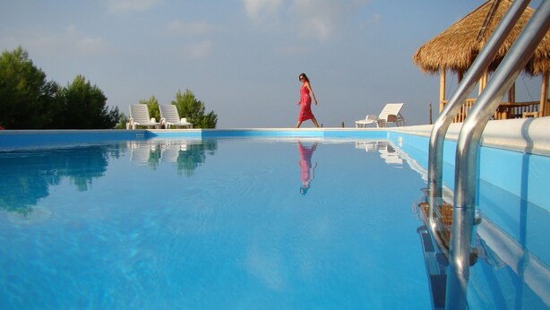 A clear blue pool with lounge chairs and a thatched-roof structure.