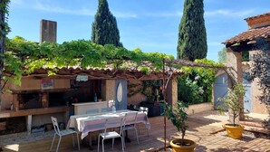 Un comedor al aire libre de estilo rústico con una mesa y sillas, rodeado de macetas con plantas y una pérgola cubierta de hiedra.