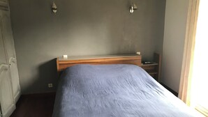 Un dormitorio con cabecera de madera, una cama individual con colcha azul, dos mesitas de noche fijadas a la pared y una lámpara de noche.