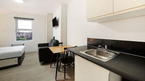 A compact kitchen with a black countertop, stainless steel sink, and a window with a view of houses. - Modern Studio in London near Wimbledon Park (London)