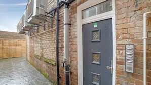 A brick building with a gray door, a keypad lock, and a window with a diamond pattern. - Modern Studio in London near Wimbledon Park (London)