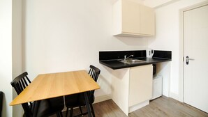 A compact kitchen with a wooden table and chairs, a black countertop, and a white door. - Modern Studio in London near Wimbledon Park (London)