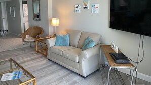 A living room with a sofa, a wicker chair, a glass coffee table, a lamp, a TV, and a small table with a laptop. - Beachfront 2Br, 2 Bath at Dunes of Panama- Sleeps 8  (3 pools, one heated) (Panama City Beach)