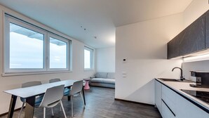Une cuisine moderne dotée d’une cuisinière intégrée, d’un coin repas avec une table et des chaises, et de grandes fenêtres laissant entrer la lumière naturelle.