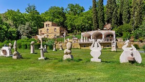 A garden with various sculptures and a stone building in the background.