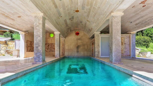 A swimming pool with a clear blue water, surrounded by stone pillars and a wooden ceiling.