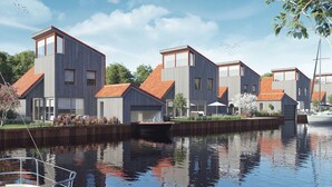 Een modern wooncomplex met meerdere huizen langs een kanaal, met grote ramen en een combinatie van houten en metalen gevels.