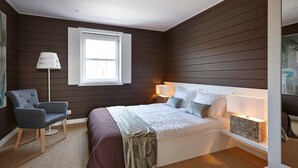 Een slaapkamer met een groot bed, een stoel, een lamp en een raam.