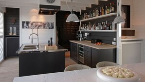 Een moderne keuken met een centraal eiland, een barruimte met drankflessen en een eethoek met een witte tafel en stoelen.