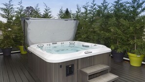 Een hottub op een houten terras, met een zonnescherm, omgeven door plantenpotten.