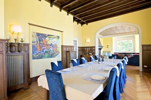 Un comedor con una mesa larga dispuesta para una comida, sillas tapizadas en azul y un cuadro grande en la pared.