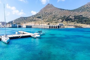 A coastal marina with boats docked, a prominent hill in the background, and buildings with arches.