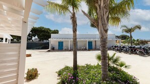 A white building with blue doors, a parking area with motorcycles, and a palm tree. - Villa in Favignana with Pool & Near the Sea (Favignana)