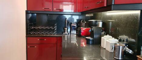 A compact kitchen with red cabinets, stainless steel countertops, and various kitchen appliances including a kettle, pots, and a coffee maker.