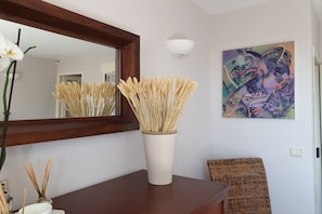 A room with a mirror, a vase with dried wheat stalks, a wicker chair, and a wall-mounted abstract painting. - Picturesque holiday home with private pool (Seillans)