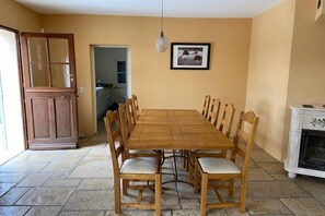 Un coin repas avec une table et des chaises en bois, une porte donnant sur la cuisine et une cheminée.