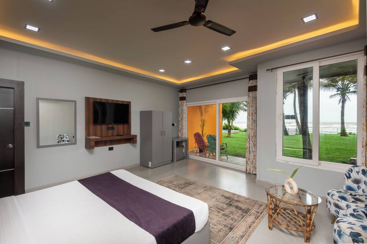 A modern bedroom with a bed, a ceiling fan, a TV, and a large window with a view of the outdoors.