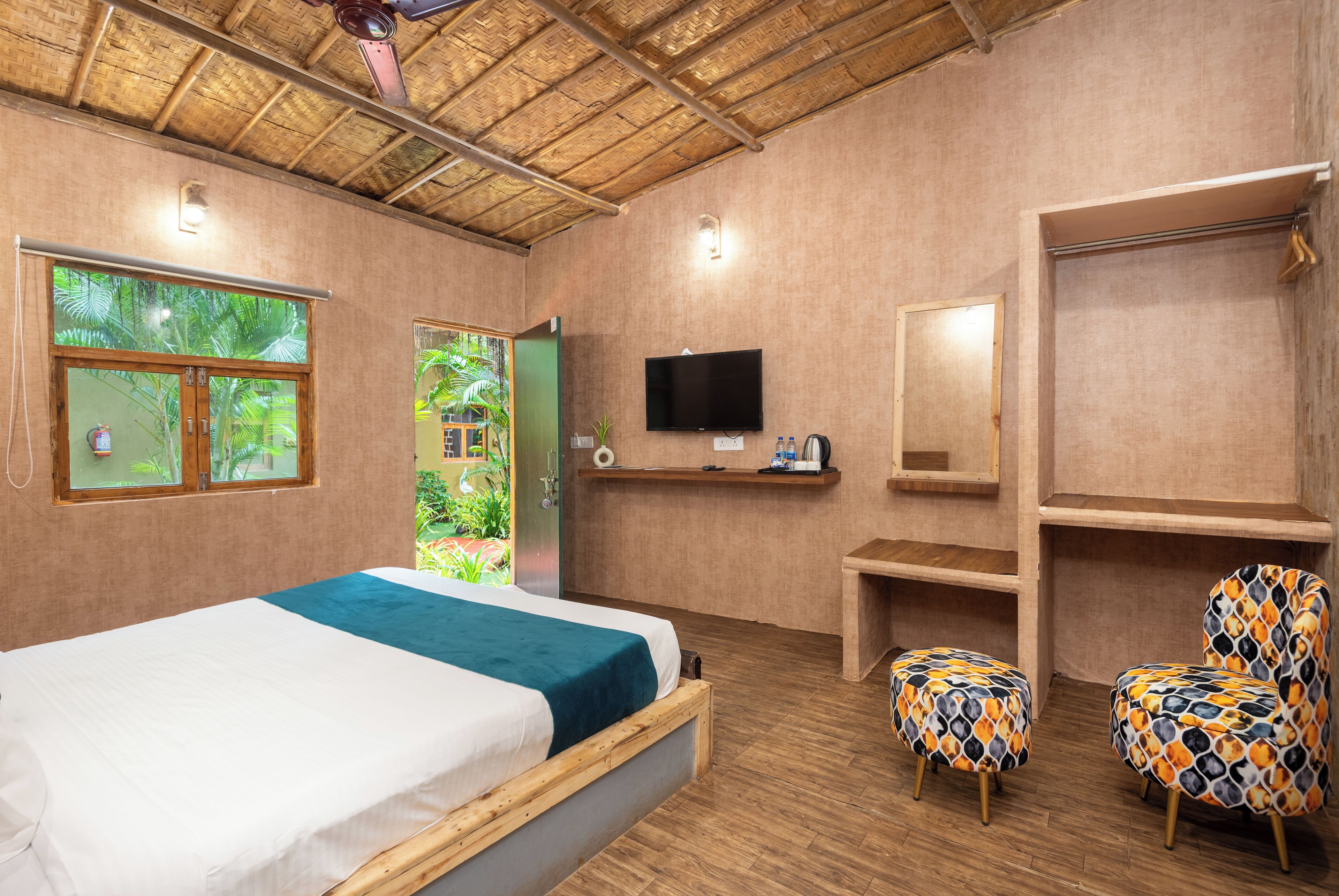 Una habitación con una cama, televisión, espejo y ventana con vistas a follaje.