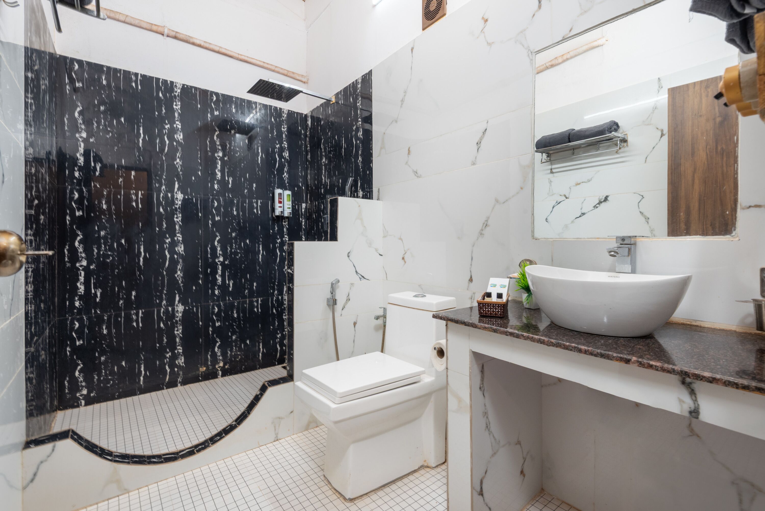 A modern bathroom with a black and white marble wall, a white toilet, a sink with a marble countertop, and a mirror above the sink.